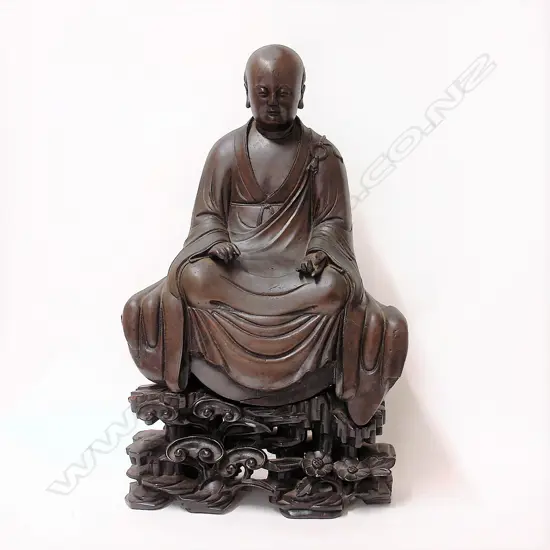 An 19thC or earlier Chinese bronze seated monk on carved wooden stand