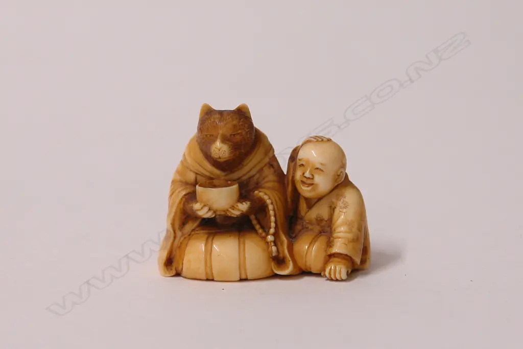 An early 20thC finely carved ivory netsuke of Tanuki seated with child Image 1++