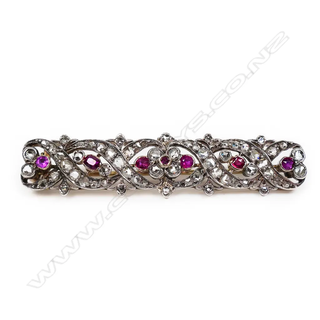 A late 19thC high carat gold, diamond and ruby brooch long rectangular form open work scrolls and floral designs festooned with graduating diamonds and highlighted with seven old facet cut rubies. Testing as 20ct. L.550mm. Image 1++