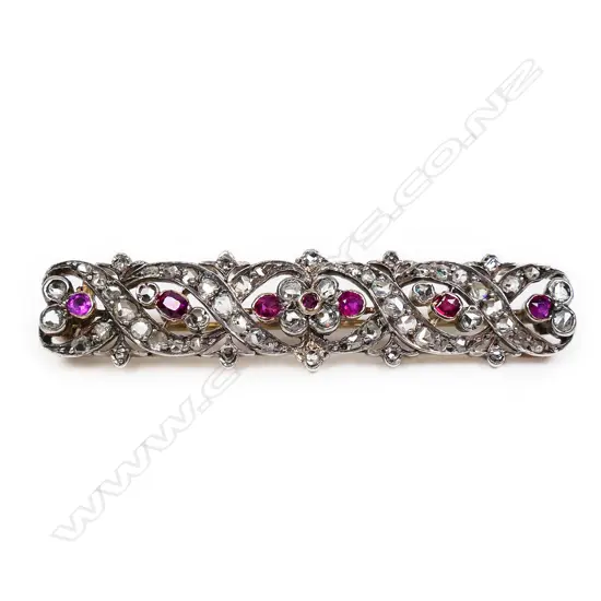 A late 19thC high carat gold, diamond and ruby brooch long rectangular form open work scrolls and floral designs festooned with graduating diamonds and highlighted with seven old facet cut rubies. Testing as 20ct. L.550mm.