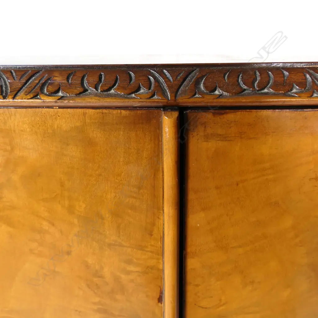 A c.1950 quality figured pale walnut drinks cabinet with the two bow front doors enclosing a mirrored back and base and with two glass shelves. Raised on cabriole legs with acanthus carved knees. 860 x 490 x 1480mm. Provenance: From the collection of Gerry and Valerie Bermel (of Travis Antiques, Wellington 1950's to 1986). Image 1++