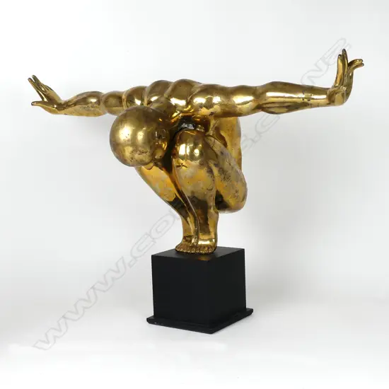 A polished bronze statue of a man in balanced toe stand pose