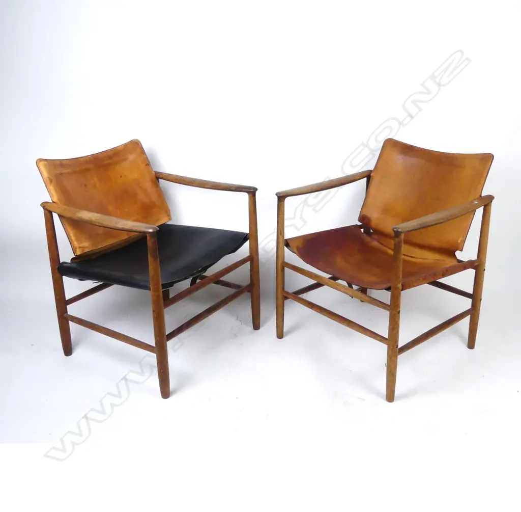 A pair of teak framed armchairs with aged leather seats and pivot mounted backs Image 1++