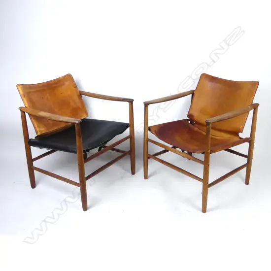 A pair of teak framed armchairs with aged leather seats and pivot mounted backs