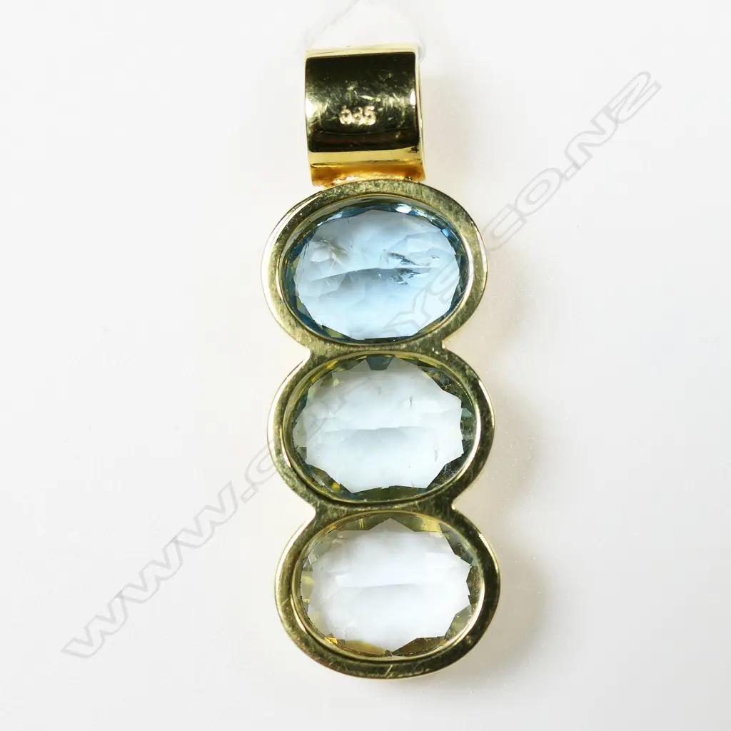 A 14ct yellow gold and blue topaz modern design pendant and ring set - the pendant with three large oval facet cut blue topaz each with rub-over mount set in a vertical row with tubular suspension above. The ring of conforming plain design with single emerald cut blue topaz in rub-over mount. 8.93gms and 5.83gms. 14.76gms total. Image 1++