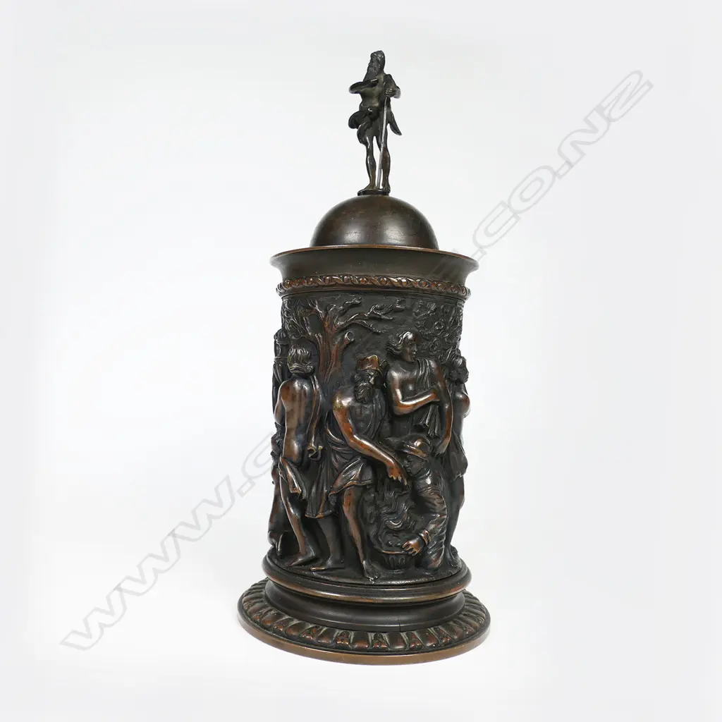 A sculptural bronze tankard - decorated in relief of a Bacchanalian feast, figural handle and male figure to the lid. H.270mm. Image 1++