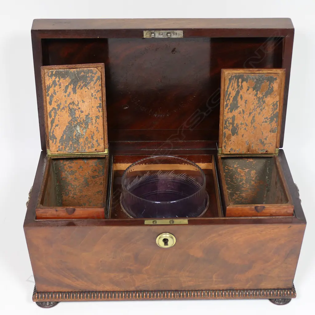 A Regency flame mahogany tea caddy - of sarcophagus form with lion mask captured ring handles, fitted interior with twin lidded compartments and period cut glass mixing bowl. 320 x 180 x 190mm, Image 1++