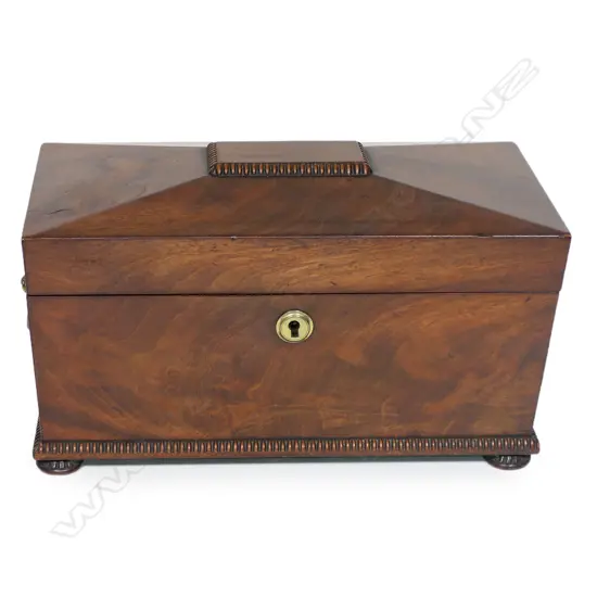 A Regency flame mahogany tea caddy - of sarcophagus form with lion mask captured ring handles, fitted interior with twin lidded compartments and period cut glass mixing bowl. 320 x 180 x 190mm,