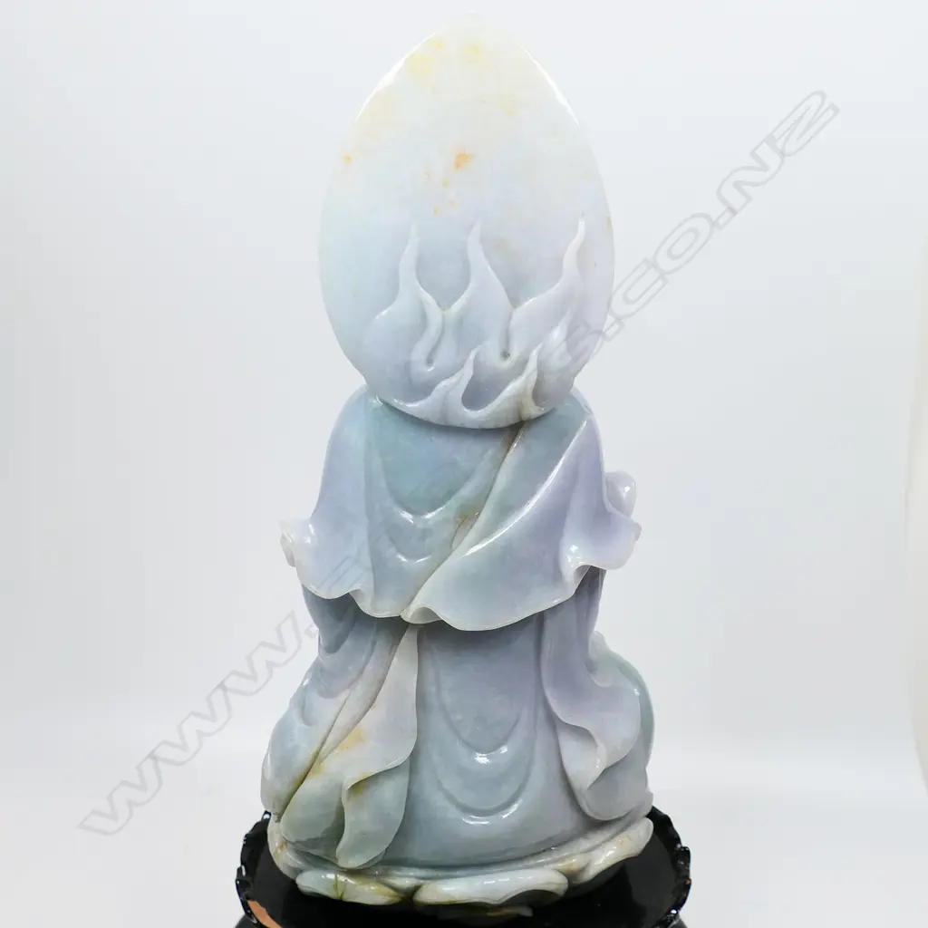 A Chinese pale jade Kuanyin statuette, pale celadon with subtle lavender tints - modelled seated upon a single lotus throne, the bodhisattva sits with left hand in vitarka mudra and right hand holding a vase with willow branch, the deities headdress covering a lotus diadem and backed by a leaf shaped mandala. On black lacquered plinth (chipped). Overall H.355mm. Image 1++