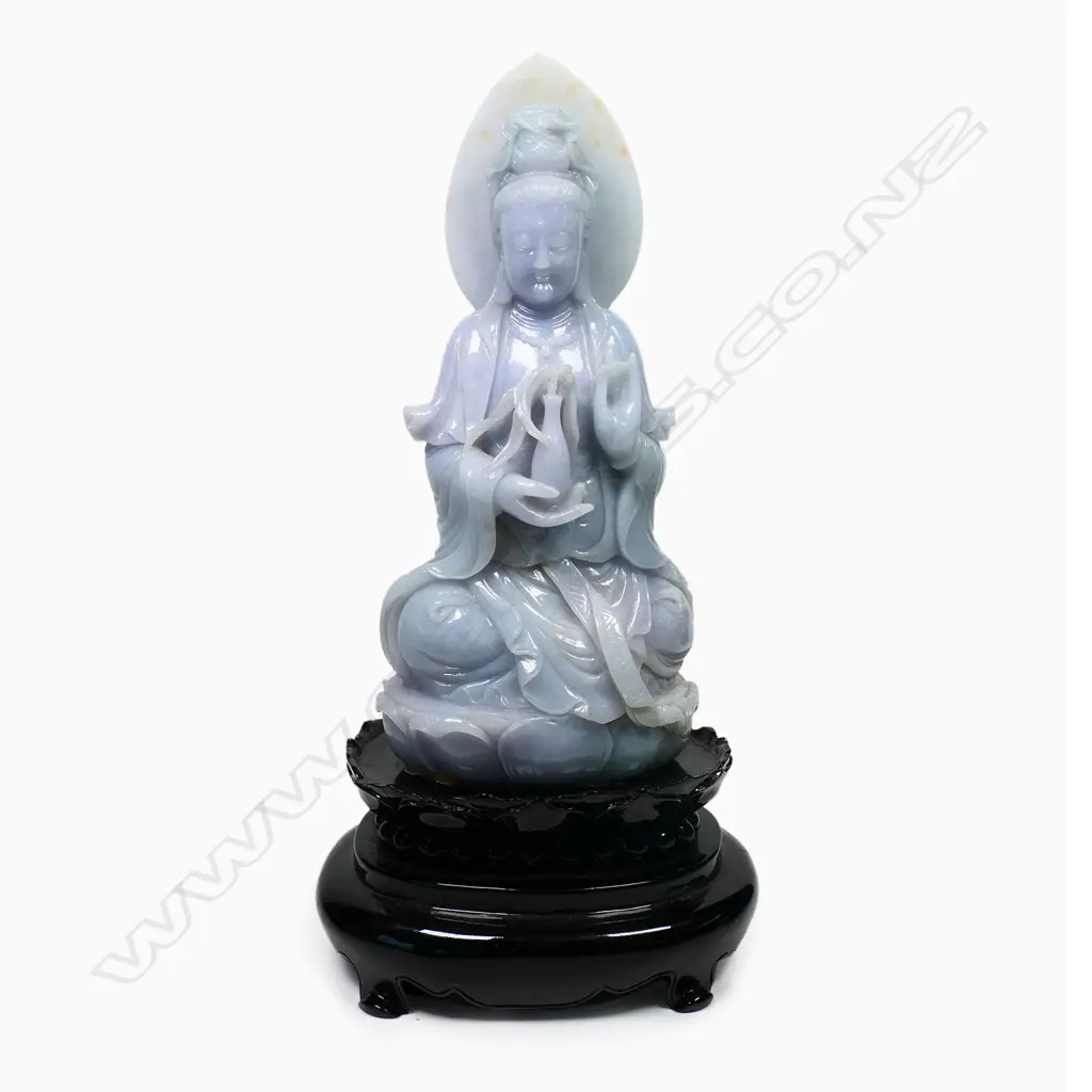 A Chinese pale jade Kuanyin statuette, pale celadon with subtle lavender tints - modelled seated upon a single lotus throne, the bodhisattva sits with left hand in vitarka mudra and right hand holding a vase with willow branch, the deities headdress covering a lotus diadem and backed by a leaf shaped mandala. On black lacquered plinth (chipped). Overall H.355mm. Image 1++