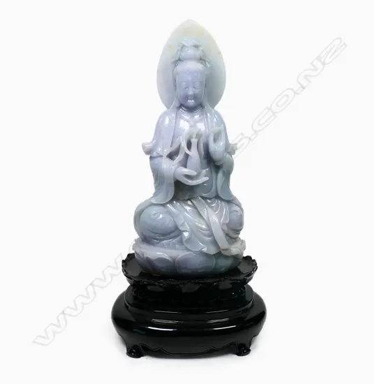 A Chinese pale jade Kuanyin statuette, pale celadon with subtle lavender tints - modelled seated upon a single lotus throne, the bodhisattva sits with left hand in vitarka mudra and right hand holding a vase with willow branch, the deities headdress covering a lotus diadem and backed by a leaf shaped mandala. On black lacquered plinth (chipped). Overall H.355mm.