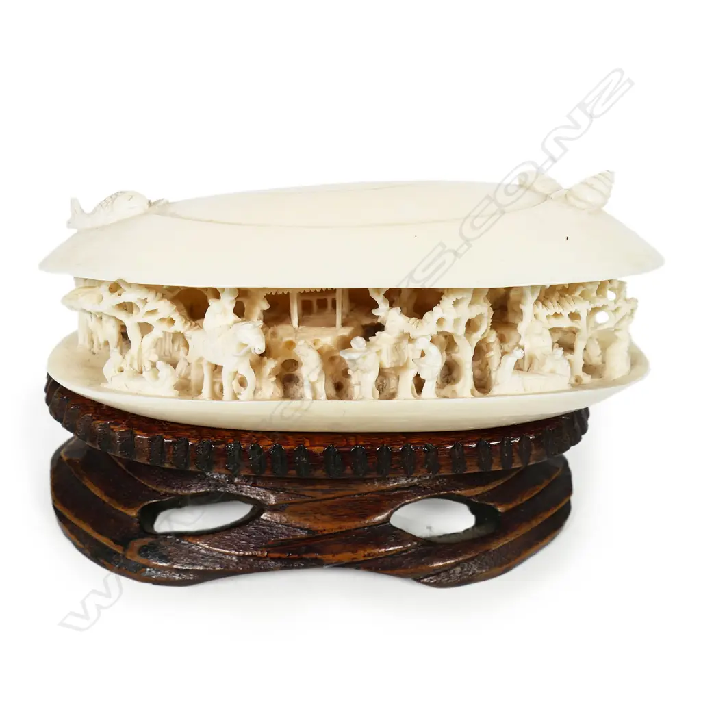 A Chinese carved ivory dream shell - of good size, the partially open shell with scene of multiple figures, trees, pagoda and more. Sea themes to the top. On carved wood stand. W.115mm. Image 1++