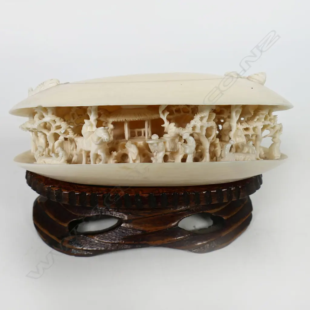 A Chinese carved ivory dream shell - of good size, the partially open shell with scene of multiple figures, trees, pagoda and more. Sea themes to the top. On carved wood stand. W.115mm. Image 1++