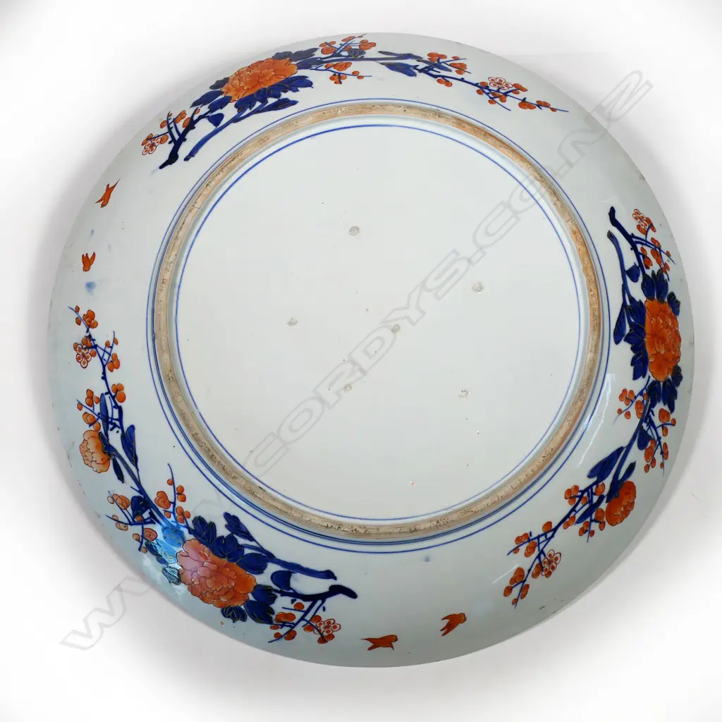 One of a matched pair, a massive Japanese Imari porcelain charger - decorated with madoe panels of 'brocade' patterns, gilt dragon rondel motifs, ancient pines and an unfurling scroll depicting Manchurian cranes in flight between ribbons of mist on a background of jade and gold cloud forms. The reverse rim painted with chrysanthemum and blossom branches in iron red and underglaze blue, Dia.600mm. Image 1++