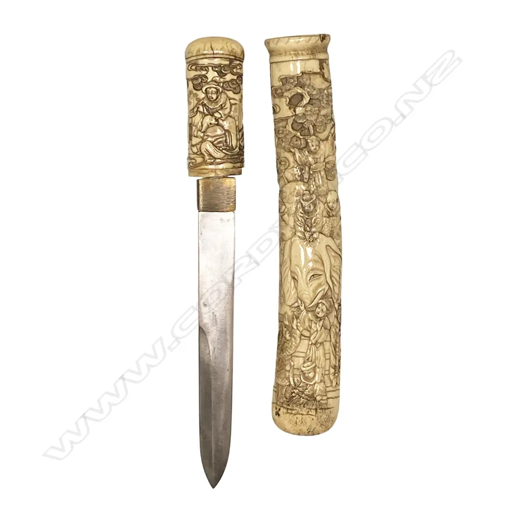 A well carved Japanese bone scabbarded and hilted tanto dagger - the scabbard carved in relief with an elephant and numerous attendants along with observers climbing a tree, the hilt with a group of figures, a small kodzuka blade inset to the scabbard. Straight blade, double edged top side for 90mm. Overall L.280mm. Image 1++
