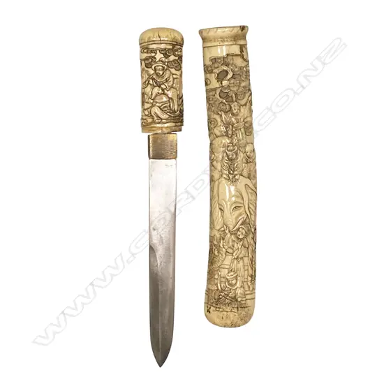 A well carved Japanese bone scabbarded and hilted tanto dagger - the scabbard carved in relief with an elephant and numerous attendants along with observers climbing a tree, the hilt with a group of figures, a small kodzuka blade inset to the scabbard. Straight blade, double edged top side for 90mm. Overall L.280mm.