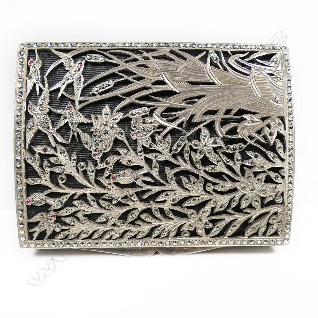 An early 20thC decorative silver box - the lid with elaborate fret cut reed, foliate and bird decorated scene jewelled with marcasite's (minor losses) and pink stones on black probably silk ground, geometric engraved Art Deco style decoration. 80 x 60 x 15mm. 118gms. Image 1++