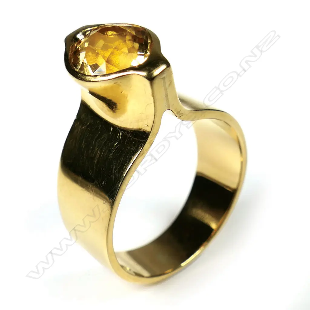 Kobi Bosshard (1939-) modernist 18ct yellow and citrine ring - c.1980's/90's, the wide plain mildly tapered band with tall raised top set with an oval facet cut citrine. Marker's mark to inside band. 11.35gms. Note: Kobi Bosshard is recognised as one of New Zealand's founding pioneer studio jewellers. Size P Image 1++