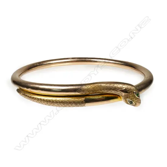 An early 20thC 9ct rose gold snake 'slave' bangle - the snake's head with emerald set eyes. Dia.86mm. 14.38gms.