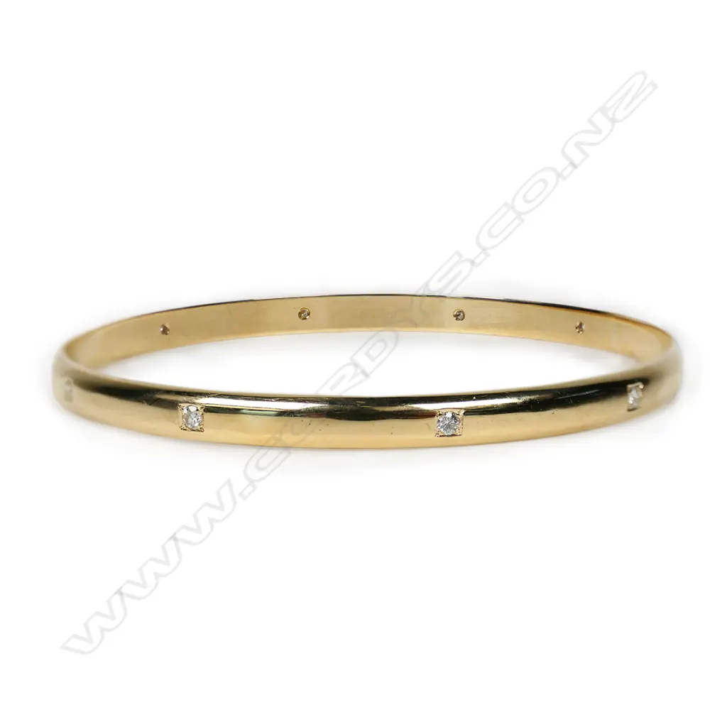 A modern 9ct yellow gold and diamond set bangle - with ten modern round brilliant cut diamonds, secured in square recessed bead settings to the half hoop bangle. TDW 0.30ct (approx). 16gms. Image 1++