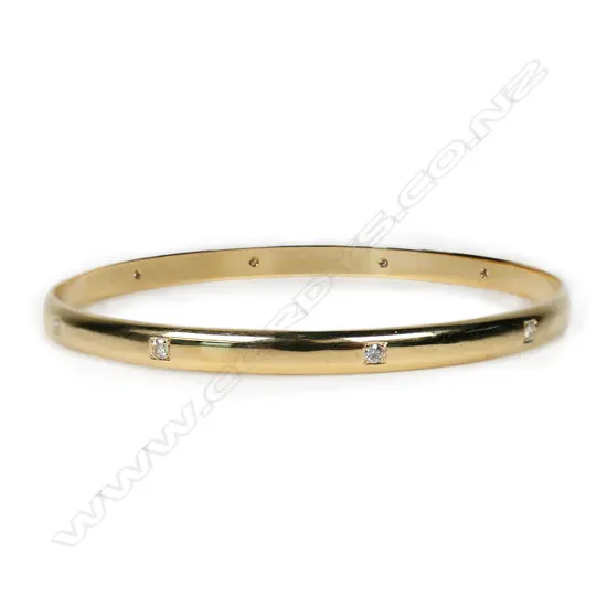 A modern 9ct yellow gold and diamond set bangle - with ten modern round brilliant cut diamonds, secured in square recessed bead settings to the half hoop bangle. TDW 0.30ct (approx). 16gms.