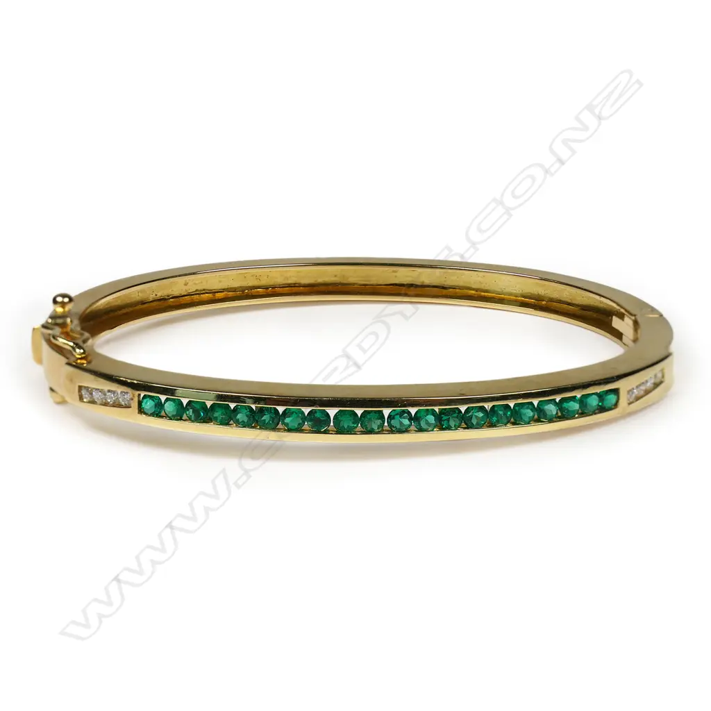 An 18ct gold, emerald and diamond hinged bangle - the top set with twenty small facet cut emeralds of top quality, set between four round brilliant cut diamonds, push clasp with two safety catches. Not marked but tests as 18ct. 15.44gms. Image 1++