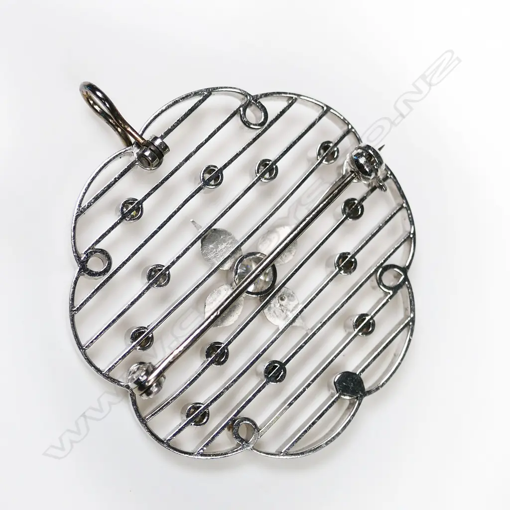 An 18ct white gold and diamond pendant/brooch - the circular flower shaped frame has interior loops with connecting horizontal bars set with small round brilliant cut diamonds (Colour G-I, Clarity VS-SI), to the centre of the frame are four diamond set petals with a 0.25ct round brilliant cut diamond to the centre (Colour H-I, Clarity SI1). TDW. 0.75ct. Pin to wear as a brooch and hinged loop to wear as a pendant. Image 1++