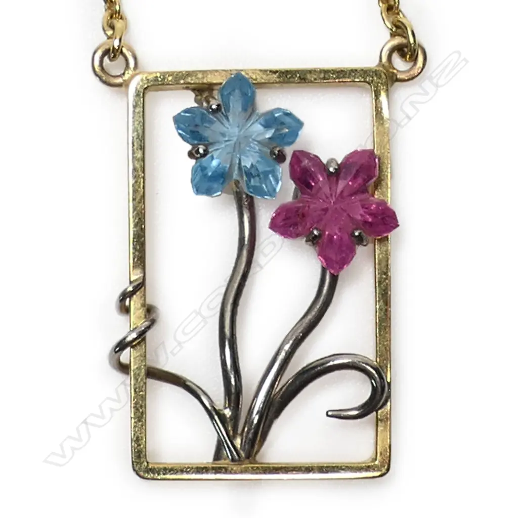 An 18ct gold modern designer pendant necklace - the rectangular open pendant with white gold restrained floral design set with a fantasy cut blue tourmaline and a pink sapphire as the flower heads. suspended on an 18ct gold chain. 11.34gms. Image 1++