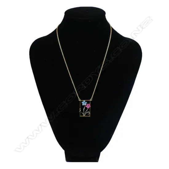 An 18ct gold modern designer pendant necklace - the rectangular open pendant with white gold restrained floral design set with a fantasy cut blue tourmaline and a pink sapphire as the flower heads. suspended on an 18ct gold chain. 11.34gms.