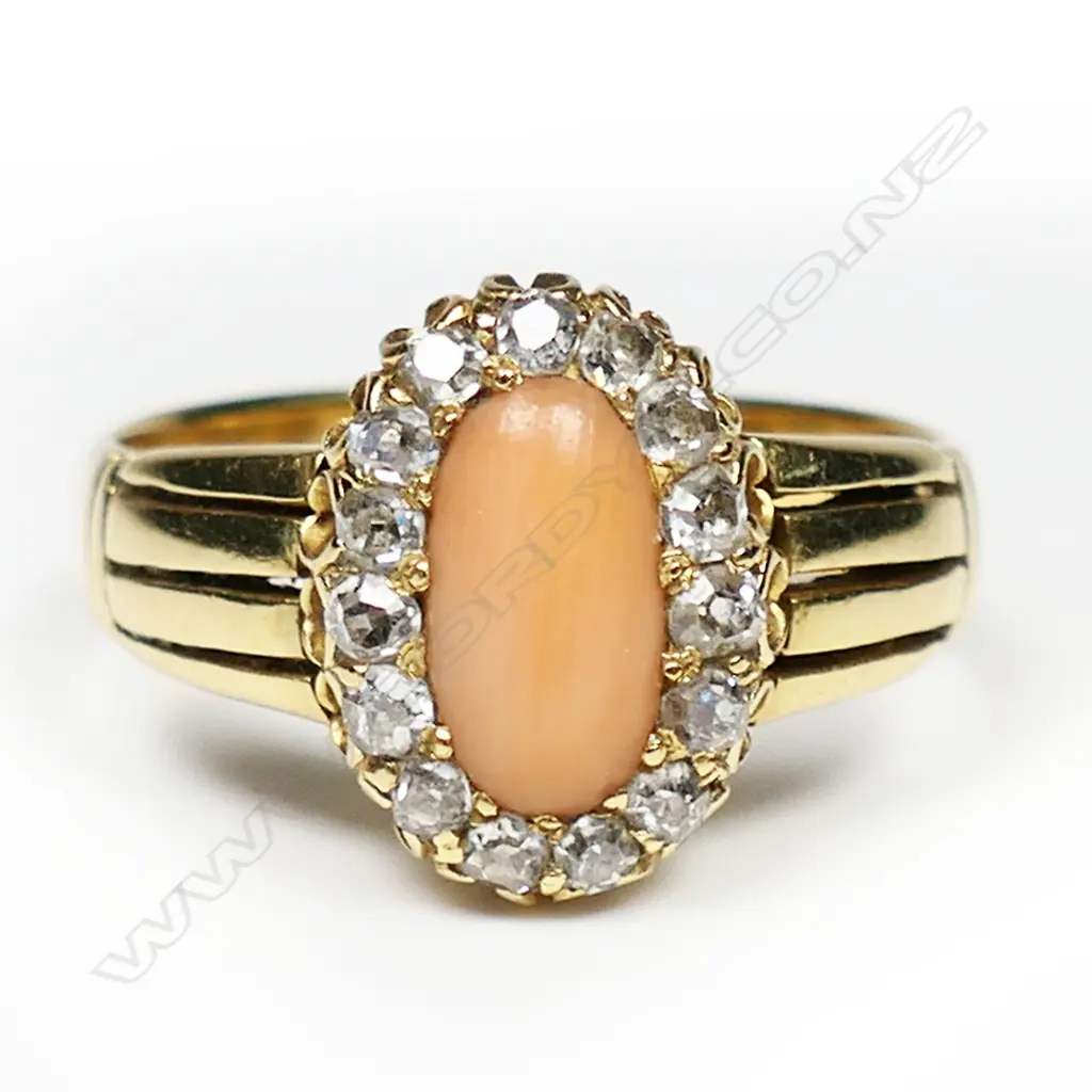 An 18ct gold coral and diamond ring - a 0.60ct medium salmon pink oval coral cabochon claw set and surrounded by fifteen old single cut diamonds (Colour H-J, Clarity VS-SI), grain set, split four bar and cuff shoulders. TDW. 0.45ct. Image 1++