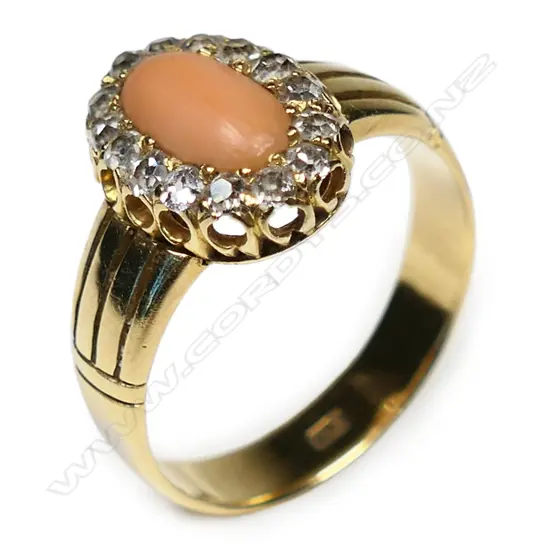 An 18ct gold coral and diamond ring - a 0.60ct medium salmon pink oval coral cabochon claw set and surrounded by fifteen old single cut diamonds (Colour H-J, Clarity VS-SI), grain set, split four bar and cuff shoulders. TDW. 0.45ct.