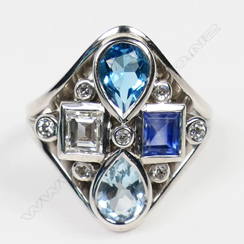 A 14ct white gold diamond, sapphire, topaz and aquamarine dress ring - the diamond form mount set with a 0.53ct rectangular step cut diamond, a 0.69ct rectangular step cut sapphire, a 0.71ct pear cut topaz and a 0.83ct pear cut aquamarine. Seven small diamonds (TDW.0.12ct) embellish the design. Maker's mark for Blooms Fine Jewellery. Valuation available. Image 1++
