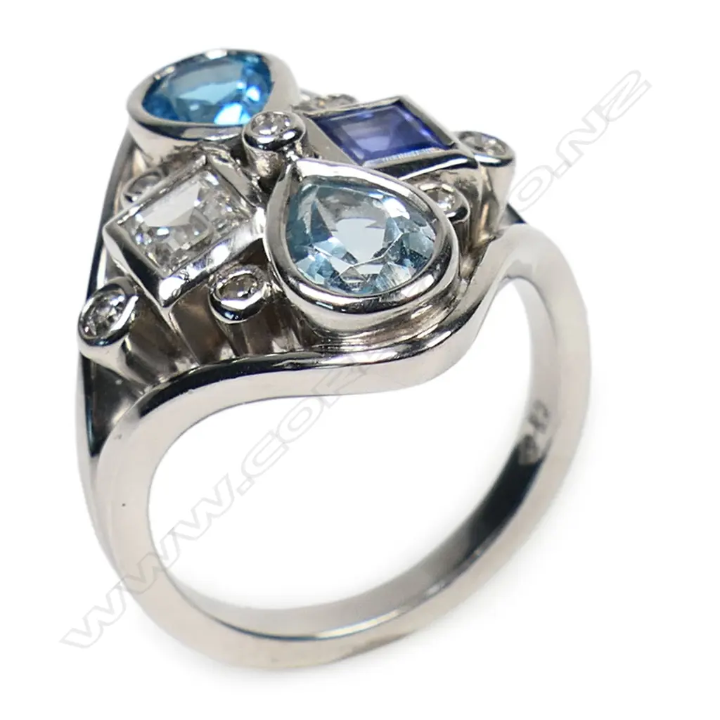 A 14ct white gold diamond, sapphire, topaz and aquamarine dress ring - the diamond form mount set with a 0.53ct rectangular step cut diamond, a 0.69ct rectangular step cut sapphire, a 0.71ct pear cut topaz and a 0.83ct pear cut aquamarine. Seven small diamonds (TDW.0.12ct) embellish the design. Maker's mark for Blooms Fine Jewellery. Valuation available. Image 1++