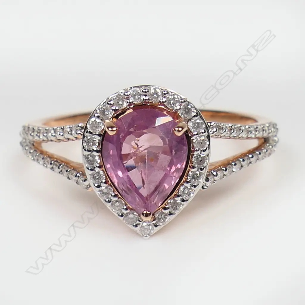 A 14ct rose gold pink sapphire and diamond halo ring - a 1.54ct pear cut orangish-pink sapphire (minor eye visible inclusions), claw set and surrounded by a halo of round brilliant cut diamonds (Colour J-K, Clarity SI2-I2), bead set in white gold with further diamonds to the split shoulders. TDW. 0.27ct. Ring size N. Image 1++