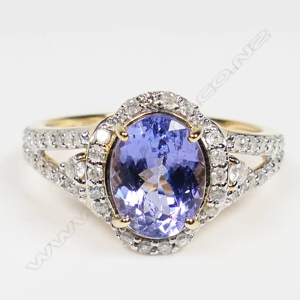 A 14ct gold tanzanite and diamond halo ring - a 1.72ct oval cut purplish-blue tanzanite (minor eye visible inclusions), claw set and surrounded by a halo of round brilliant cut diamonds (Colour J-K, Clarity SI2-I2), bead set, with further diamonds to the split shoulders. TDW. 0.33ct. Ring size M. Image 1++