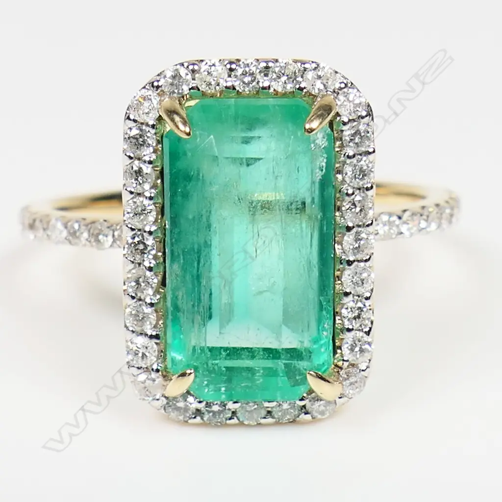 A 14ct gold Colombian emerald and diamond halo cocktail ring - a 3.80ct emerald cut strong bright green Colombian emerald (moderate natural inclusions), claw set and surrounded by a halo of round brilliant cut diamonds (Colour G-I, Clarity SI1-I2) micro claw set in white gold, with further diamonds to each shoulder. TDW. 0.43ct. Ring size N. Image 1++