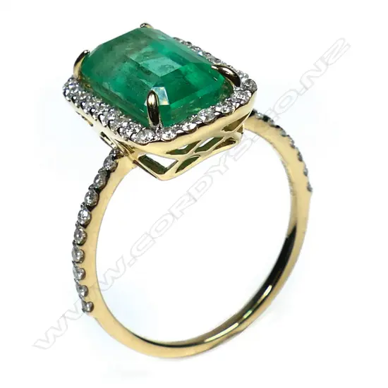 A 14ct gold Colombian emerald and diamond halo cocktail ring - a 3.80ct emerald cut strong bright green Colombian emerald (moderate natural inclusions), claw set and surrounded by a halo of round brilliant cut diamonds (Colour G-I, Clarity SI1-I2) micro claw set in white gold, with further diamonds to each shoulder. TDW. 0.43ct. Ring size N.