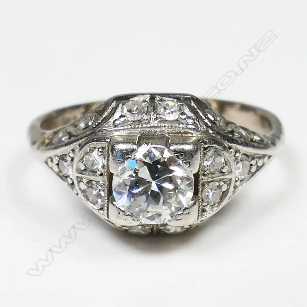 An Art Deco platinum and solitaire diamond ring - the approx. 0.45ct old brilliant cut diamond secured by four bracket corner claws with 10 further small diamonds bead set to the scroll pierced mount. Image 1++
