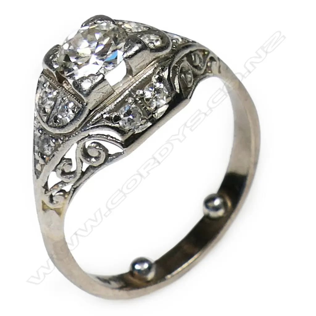 An Art Deco platinum and solitaire diamond ring - the approx. 0.45ct old brilliant cut diamond secured by four bracket corner claws with 10 further small diamonds bead set to the scroll pierced mount. Image 1++