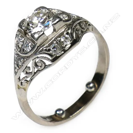 An Art Deco platinum and solitaire diamond ring - the approx. 0.45ct old brilliant cut diamond secured by four bracket corner claws with 10 further small diamonds bead set to the scroll pierced mount.