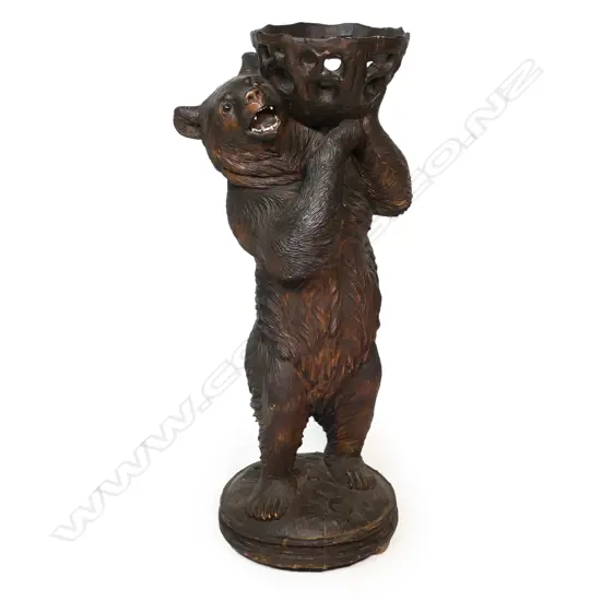 A late 19thC Black Forest carved large floor standing bear with basket - he stands holding aloft a pierced and carved branch form basket. His open mouth with carved and white painted teeth, glass set eyes. On circular domed base with further carved naturalistic detail. H.945mm.