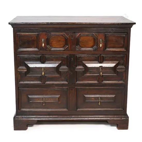An oak William and Mary style three drawer chest - geometric panels to the drawers, hanging brass handles, raised on bracket feet. 970 x 560 x 900mm.
