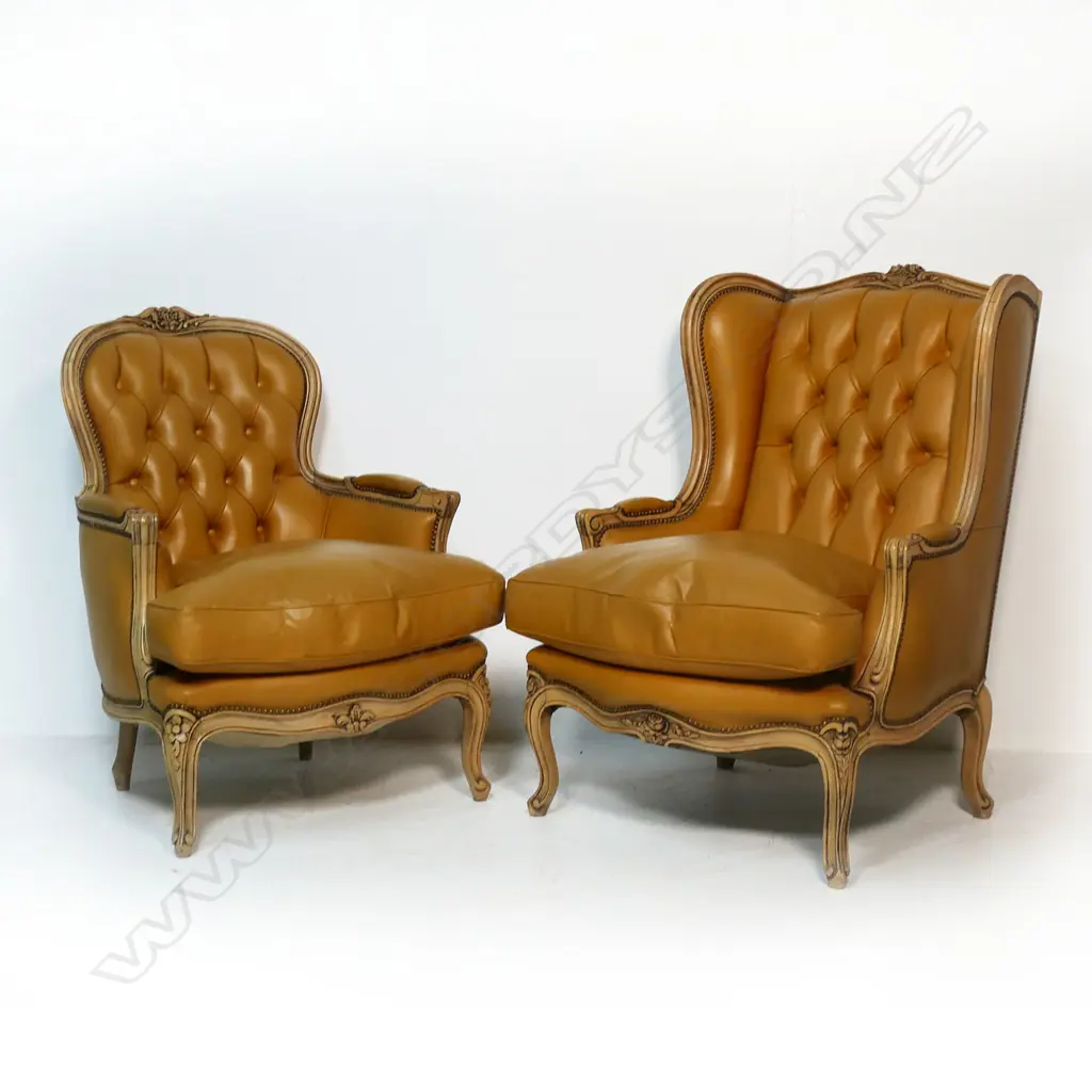 Two matching modern antique French style leather armchairs - one a wing back, the other a fauteuil, the similar chairs with carved frames, buttoned back upholstery in tan leather. Image 1++