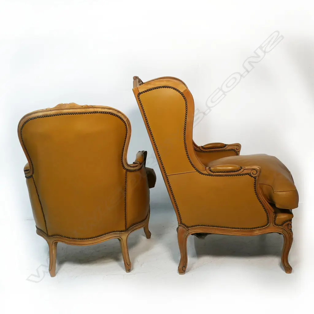 Two matching modern antique French style leather armchairs - one a wing back, the other a fauteuil, the similar chairs with carved frames, buttoned back upholstery in tan leather. Image 1++
