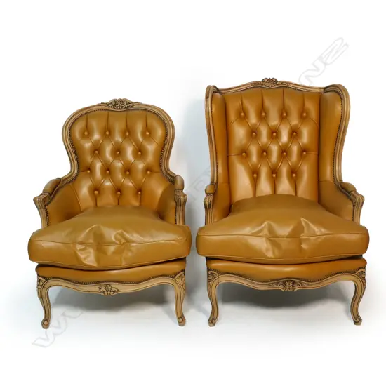 Two matching modern antique French style leather armchairs - one a wing back, the other a fauteuil, the similar chairs with carved frames, buttoned back upholstery in tan leather.
