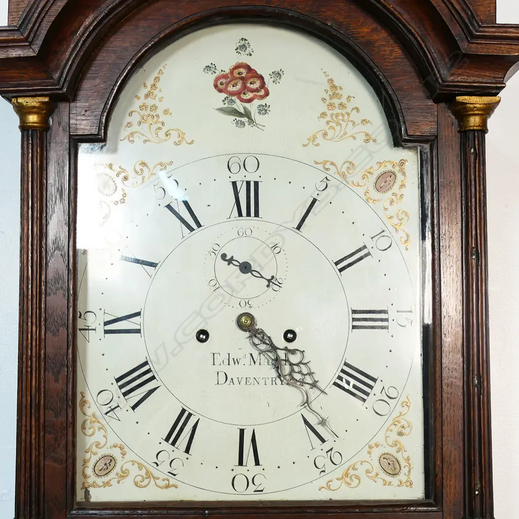 A Georgian oak long case clock - the hood with two finials, (one absent), reeded column with brass detail to each side, the dial with painted floral decoration, Roman numerals with the minutes in Arabic numerals, seconds dial, marked Edwd. Maud, Daventry, chamfered sides to case. 460 x 240 x 2600mm. Image 1++