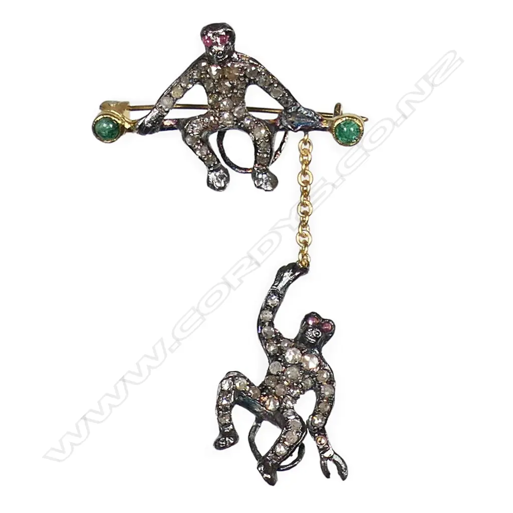 An antique style silver gilt monkey brooch a monkey sits on a branch with another hanging by a gold chain. Both monkeys embellished with rose cut diamonds, red spinel eyes and cabochon emeralds to each end of the branch. TDW. 0.50ct. TEW. 0.30ct. 3.76gms. (one diamond missing on hanging monkey). Image 1++