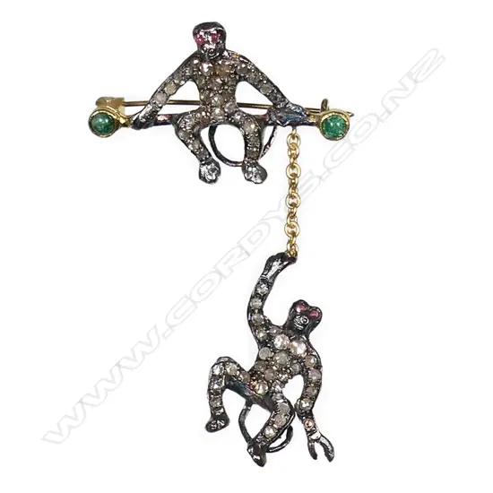 An antique style silver gilt monkey brooch a monkey sits on a branch with another hanging by a gold chain. Both monkeys embellished with rose cut diamonds, red spinel eyes and cabochon emeralds to each end of the branch. TDW. 0.50ct. TEW. 0.30ct. 3.76gms. (one diamond missing on hanging monkey).