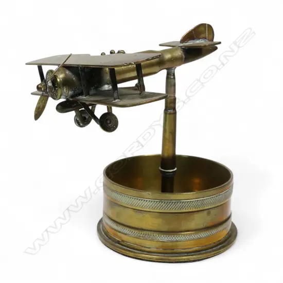 An old brass trench art float bi-plane on large shell cartridge end base,