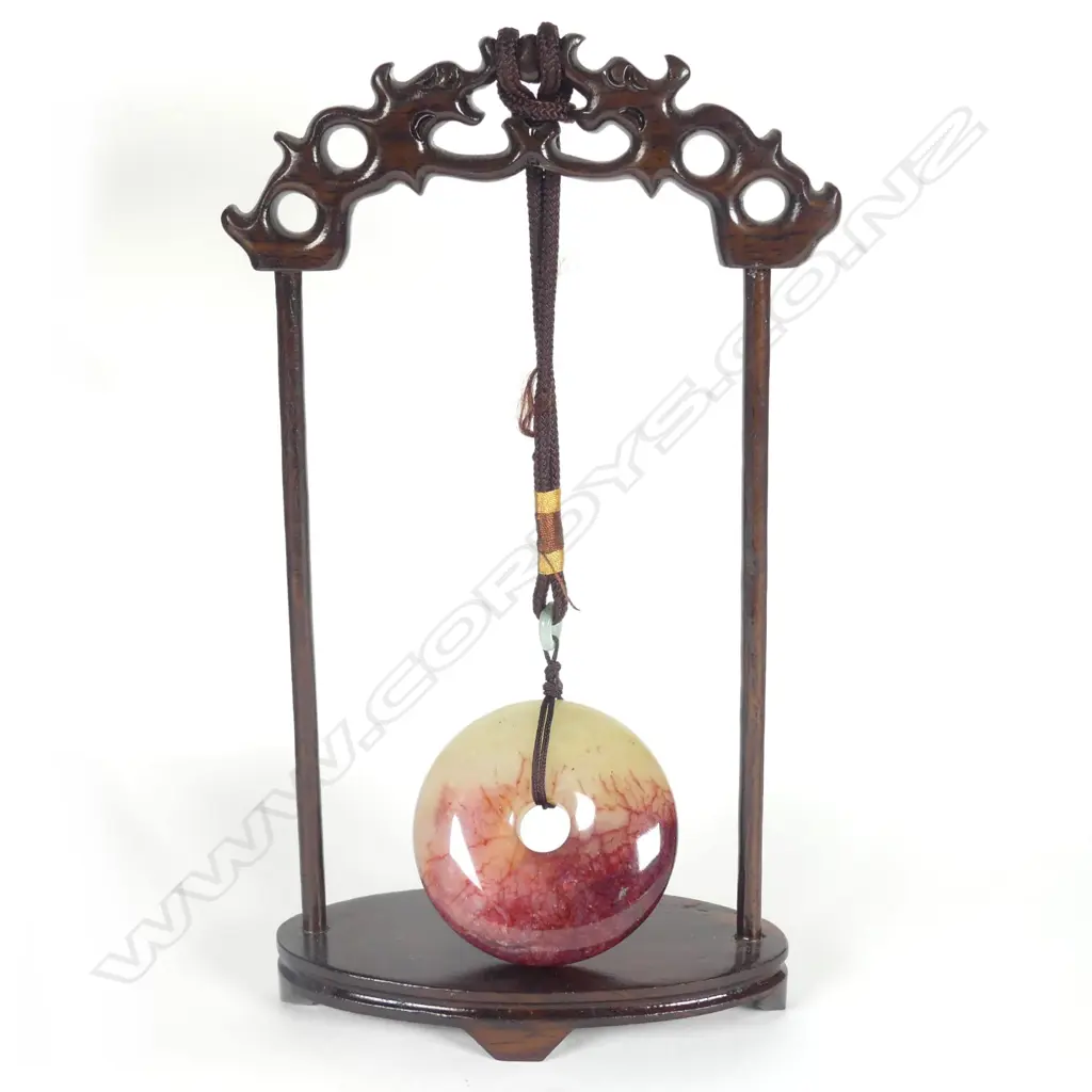 A Chinese chicken-blood jade disc suspended on wooden stand Image 1++